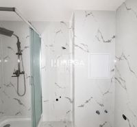 A bathroom with a shower in a two-room apartment with marble tiles.
