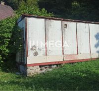 An old warehouse in the garden of a street in Humenné, surrounded by greenery and growing grass.