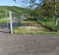 A residential plot in Humenné on a fenced street, surrounded by greenery.