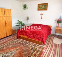 A bedroom in a family house with a red blanket, wooden furniture, and decorative flowers.