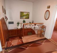 A hallway with carpets and a staircase, a floor with a wooden decor, access to the kitchen.