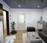 Living room with a sofa, TV, and wood-patterned flooring in a three-room apartment.