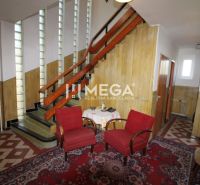 Inside the family house, there are stairs, two red armchairs, and a carpet with a geometric pattern.
