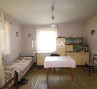 A room in a family house with wallpaper, a table, a bed, a display cabinet, and a floor with a wooden decor.