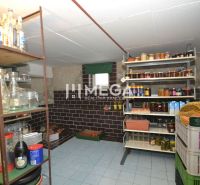 A pantry with shelves full of preserves in a family house, stone-clad walls, and a tiled floor.