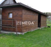 A wooden structure by a family house in the town of Krásny Brod on green grass.