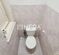 A restroom with walls lined with light tiles and a window in commercial premises.