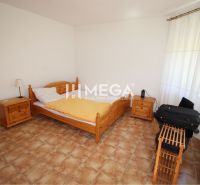 A bedroom with a bed, wooden furniture, and tiles on the floor in a family house.