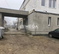 A building on SNP Street in Snina with a parked car and a container on a gravel surface.