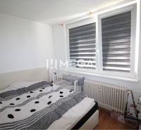 Bedroom in a two-room apartment with a radiator and a bed, floor with wooden decor.