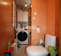 A bathroom with a washing machine and a toilet in a 2-room apartment with orange ceramic tiles.