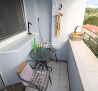 A balcony of a 2-room apartment with a café table and a view of greenery.