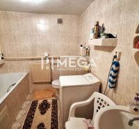 A bathroom with a white bathtub and a washing machine in a family house, tiled with light tiles.
