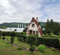A cottage in Nová Kelča surrounded by greenery with a view of the lake and hills.