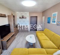Living room in a 3-room apartment with a wooden decor floor, a yellow sofa, and shelves.