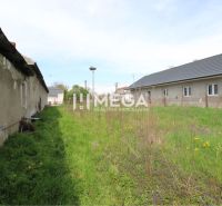 Residential plots in Senné with a dilapidated building and grassy area.