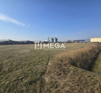 Grass and industrial premises in Hriadky under a clear sky, with an industrial building on the horizon.