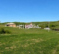 Grassy residential plots in the village of Víťazovce surrounded by green hills and buildings.