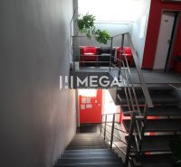 A hallway in offices with a metal railing and a red chair.