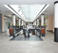 Commercial spaces with escalators and modern lighting, flooring with a wooden decor.