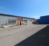 Warehouses and halls on Fidlikova Street in Humenné with stored material and a parked car.
