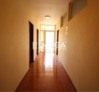 A corridor with brown flooring leading to offices with bright lighting.