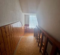 A hallway with wooden paneling and railing, a floor with a wooden decor, a window made of glass blocks.
