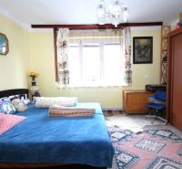 A bedroom in a family house with a blue bed, wooden furniture, and a colorful carpet.