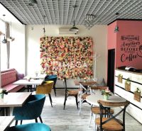 A café with a flower wall in the dining area and chairs of various colors.