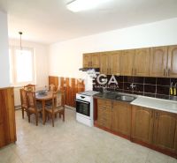 A kitchen in a family house with a dining table, wooden cabinets, and tiles.