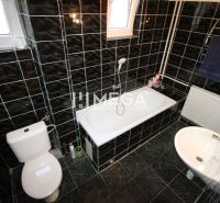 A bathroom with dark tiles and a bathtub in a family house.