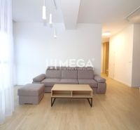 Bright living room with a corner sofa and wood-patterned flooring in a three-room apartment.