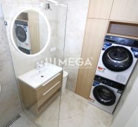 A bathroom in a 3-room apartment with a washing machine, dryer, and illuminated round mirror.