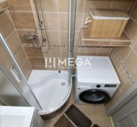 A bathroom with a shower and a washing machine in a 3-room apartment, with brown tiles.