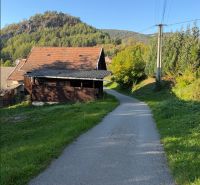 The road in Košecké Podhradie runs alongside houses, bordered by greenery and hills. Plots - residential.