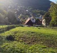 A residential plot in Košecké Podhradie surrounded by nature and houses, beneath mountain peaks.