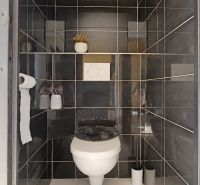 A bathroom in a three-room apartment with dark gray tiles and white sanitary ware.