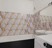 A bathroom with a bathtub and a washing machine in a 3-room apartment, tiles with a bold pattern.