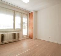 A room in a one-room apartment with a wooden decor floor, white walls, and windows.