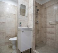 Bathroom in a studio apartment with a sink, shower, and beige tiles.