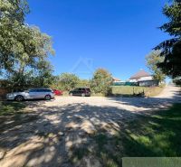 Cars are parked on a paved area near the gardens in Pastuchov under a clear blue sky.