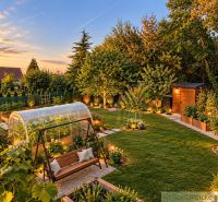 A garden with a swing bench and a greenhouse near a cottage in Nové Zámky during sunset.