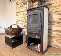 Wood-burning stove with a woven basket and a stone wall, floor with wooden decor in the cabin.