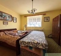 A bedroom in a family house with a bed and a furniture wall, with paintings on the wall.