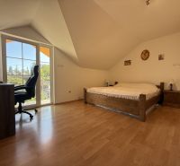 Attic bedroom in a family house with a bed, wooden decor flooring, and a desk.