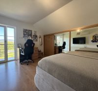 A bedroom in a family house with a wooden decor floor, a mirrored wardrobe, and balcony doors.