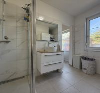 A bathroom in a family house with white tiles, a shower, and storage spaces.
