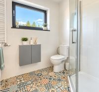 Bathroom with a shower, toilet, and window, colorful patterned tiles on the floor.