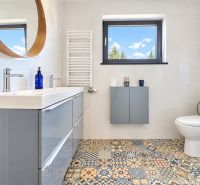 A bathroom with a mosaic floor, a modern sink, and a window in a studio apartment.