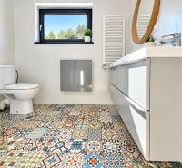 A bathroom with colorful tiles, a shower corner, and a mirror in a studio apartment.